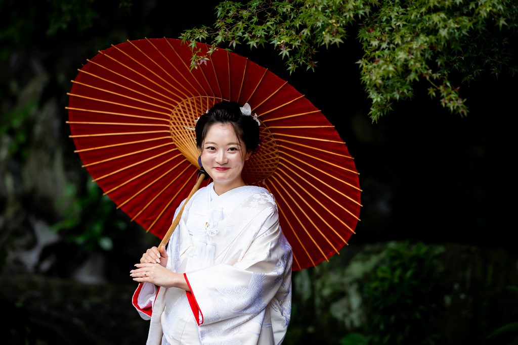 今宮神社の緑を背景に赤い番傘を持つ白無垢姿の新婦