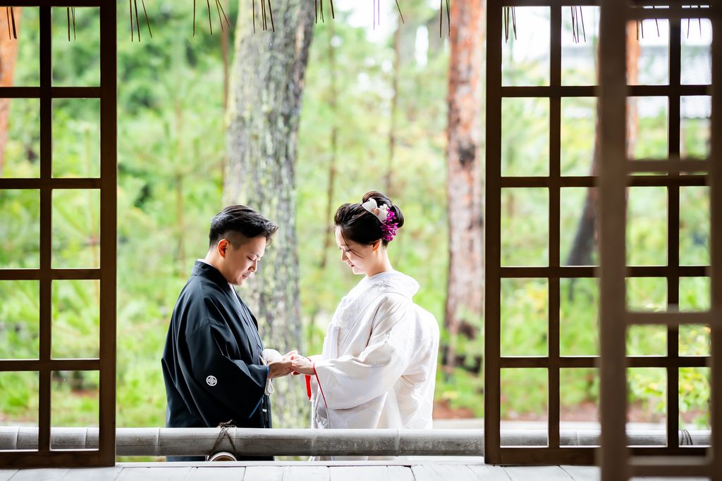 緑を背景に顔を寄せ合う白無垢の新婦と紋付袴の新郎